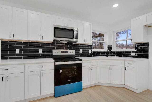 kitchen with appliances with stainless steel finishes, light wood-type flooring, backsplash, sink, and white cabinetry