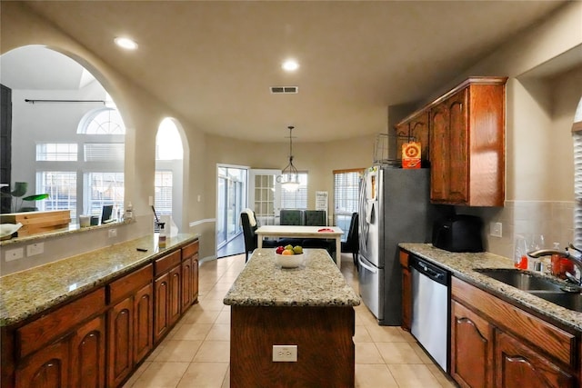 kitchen featuring sink, hanging light fixtures, stainless steel appliances, light stone counters, and a kitchen island