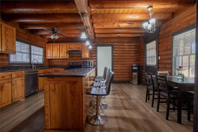 kitchen featuring pendant lighting, black appliances, beam ceiling, rustic walls, and a kitchen island