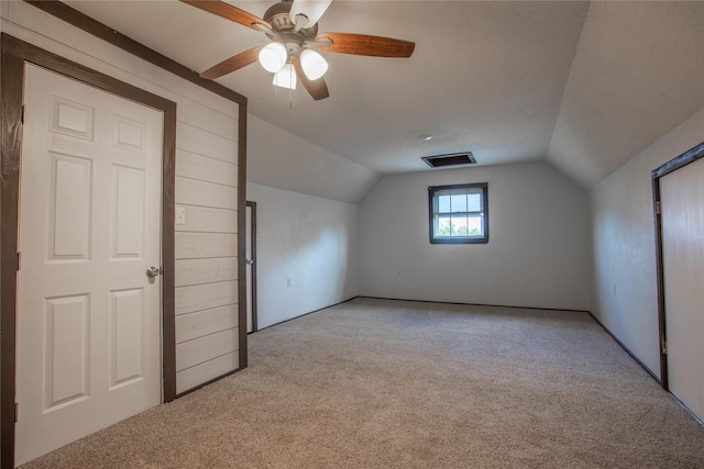 additional living space with light carpet, a textured ceiling, vaulted ceiling, and ceiling fan