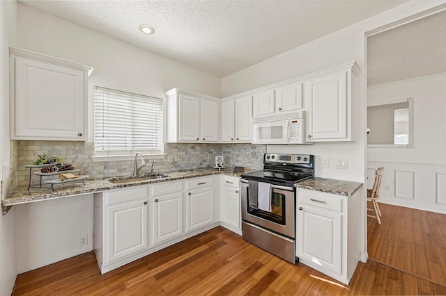 kitchen featuring sink, light stone counters, white cabinets, stainless steel electric range oven, and light wood-type flooring