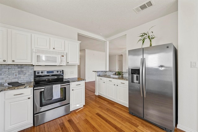 kitchen with white cabinetry, appliances with stainless steel finishes, and dark stone counters