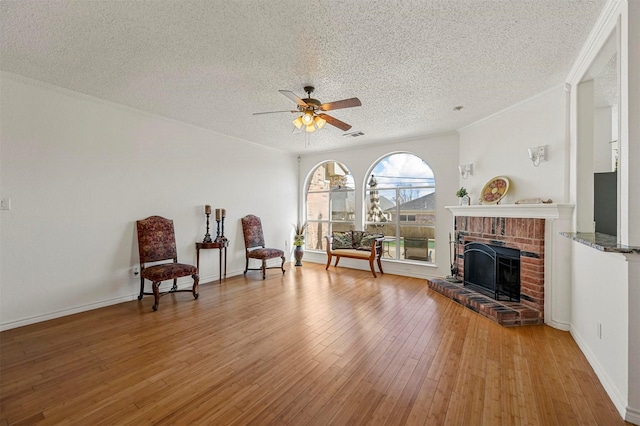 sitting room featuring ceiling fan, crown molding, a brick fireplace, a textured ceiling, and light hardwood / wood-style flooring