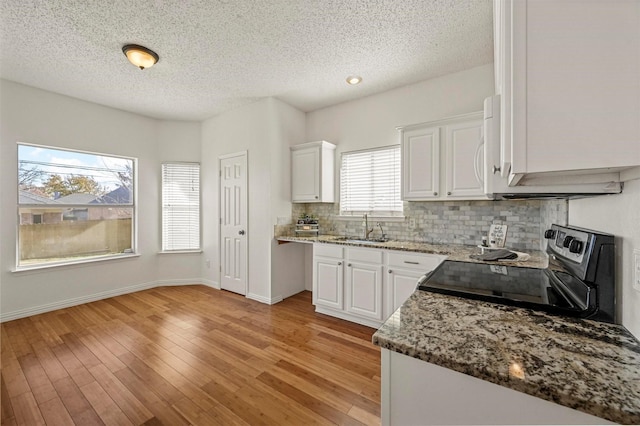 kitchen featuring sink, white cabinetry, light hardwood / wood-style flooring, range with electric cooktop, and dark stone counters