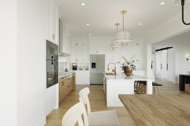 kitchen featuring white cabinetry, hanging light fixtures, a large island with sink, built in fridge, and a barn door