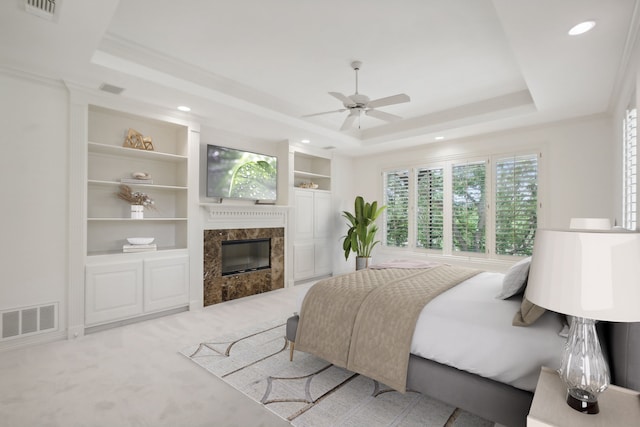 bedroom featuring a fireplace, light colored carpet, a raised ceiling, and ceiling fan