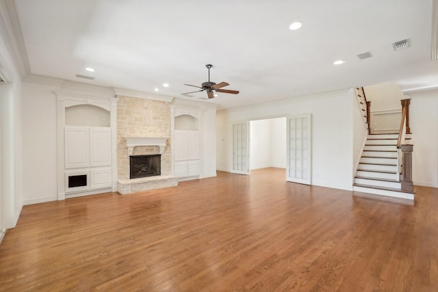 unfurnished living room featuring hardwood / wood-style floors, a stone fireplace, ceiling fan, and ornamental molding