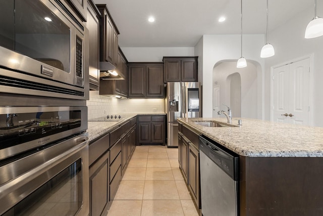 kitchen featuring sink, hanging light fixtures, appliances with stainless steel finishes, a kitchen island with sink, and decorative backsplash