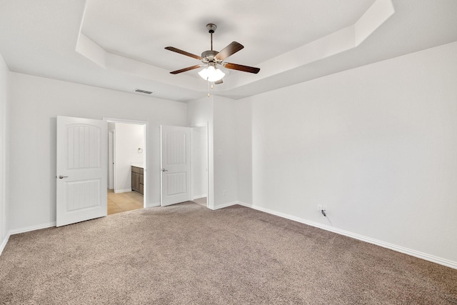 carpeted spare room with ceiling fan and a raised ceiling