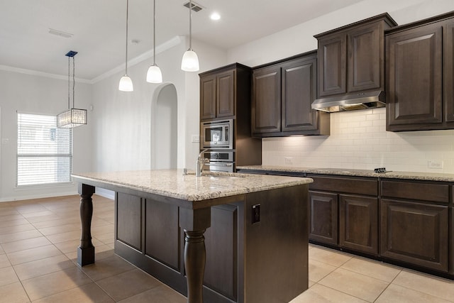 kitchen featuring appliances with stainless steel finishes, decorative light fixtures, backsplash, a kitchen island with sink, and dark brown cabinets