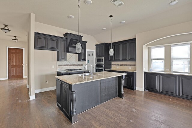 kitchen with sink, light stone counters, hanging light fixtures, a center island with sink, and appliances with stainless steel finishes