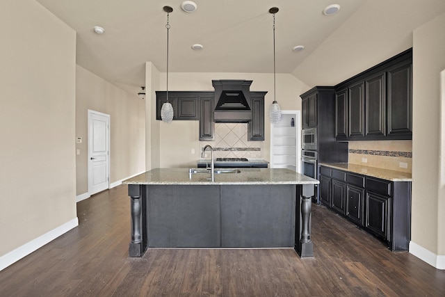 kitchen with sink, appliances with stainless steel finishes, an island with sink, decorative light fixtures, and custom exhaust hood