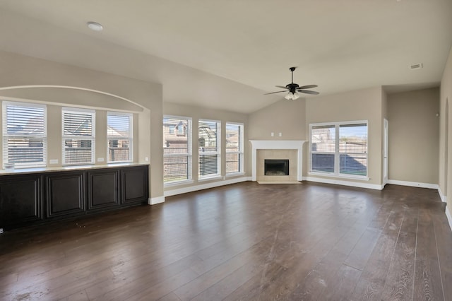 unfurnished living room with a tiled fireplace, dark wood-type flooring, ceiling fan, and vaulted ceiling