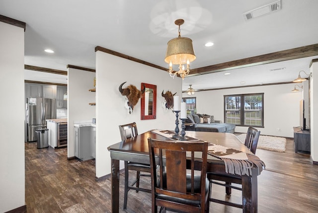 dining room featuring beverage cooler, ceiling fan with notable chandelier, visible vents, dark wood finished floors, and crown molding