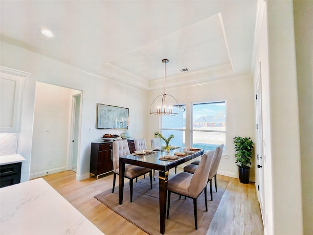 dining area featuring a notable chandelier, light hardwood / wood-style flooring, and a tray ceiling