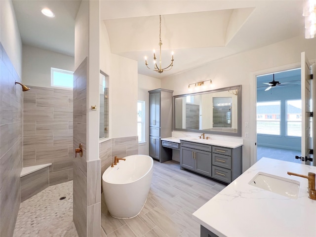 bathroom with tile walls, ceiling fan with notable chandelier, plus walk in shower, and vanity