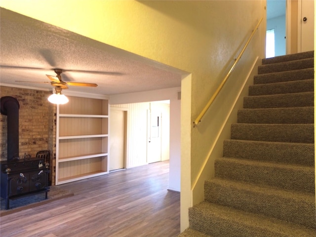 stairway with a wood stove, ceiling fan, wood-type flooring, and a textured ceiling