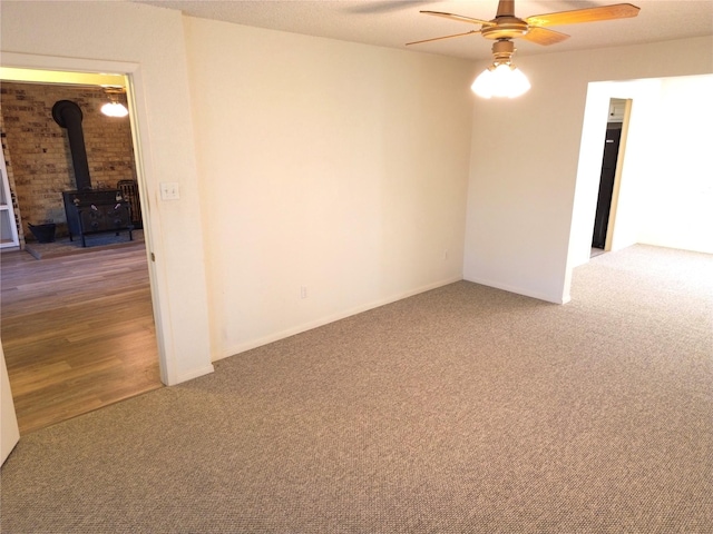 unfurnished room featuring a wood stove, ceiling fan, carpet floors, and a textured ceiling