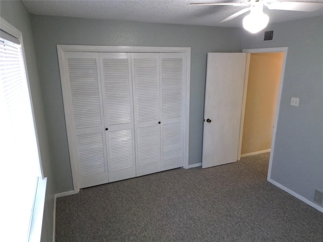 unfurnished bedroom featuring ceiling fan, a closet, dark carpet, and a textured ceiling