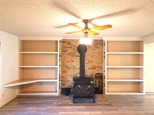 unfurnished living room featuring a wood stove, ceiling fan, wood-type flooring, and a textured ceiling