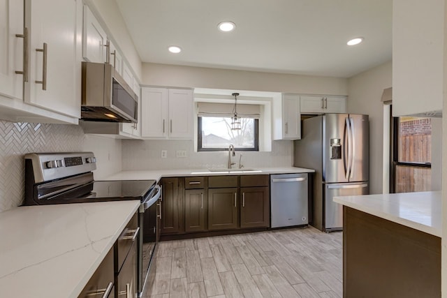 kitchen featuring white cabinets, hanging light fixtures, sink, appliances with stainless steel finishes, and light stone counters