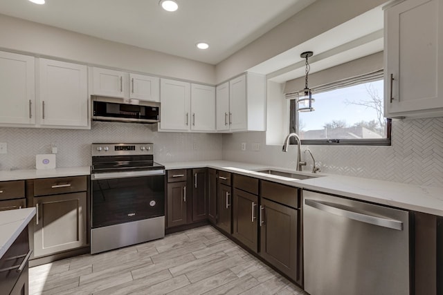 kitchen featuring light stone countertops, sink, decorative light fixtures, white cabinets, and appliances with stainless steel finishes