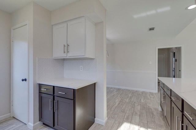 kitchen featuring decorative backsplash, light hardwood / wood-style flooring, white cabinetry, and light stone counters