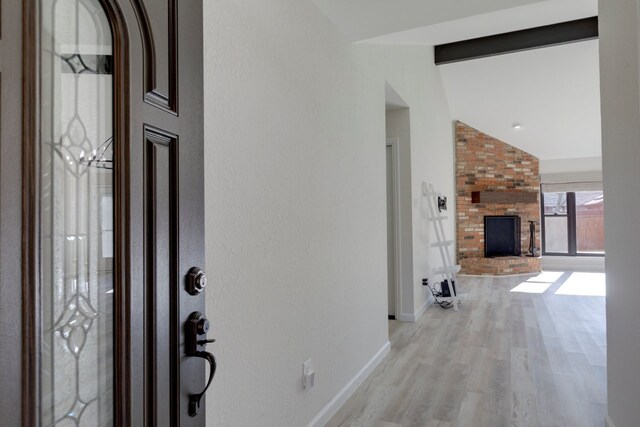 entryway featuring lofted ceiling with beams, light wood-type flooring, and a fireplace