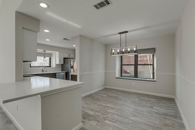 kitchen featuring gray cabinetry, hanging light fixtures, stainless steel appliances, kitchen peninsula, and light wood-type flooring