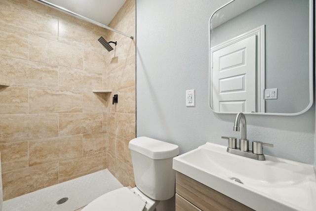 bathroom featuring a tile shower, vanity, and toilet