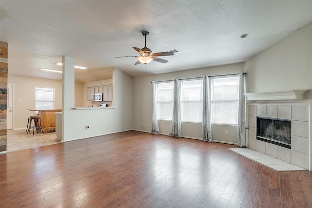 unfurnished living room with a textured ceiling, ceiling fan, light hardwood / wood-style flooring, and a tiled fireplace