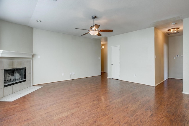 unfurnished living room featuring a tile fireplace, ceiling fan, and hardwood / wood-style floors