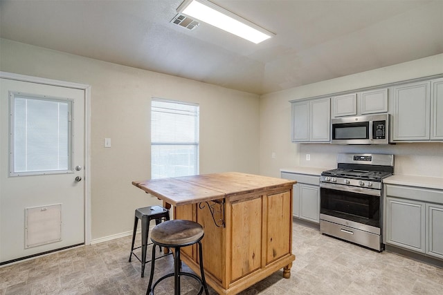 kitchen with a kitchen bar, a center island, stainless steel appliances, and gray cabinetry