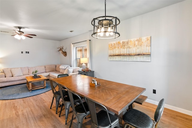 dining space with ceiling fan with notable chandelier and light wood-type flooring