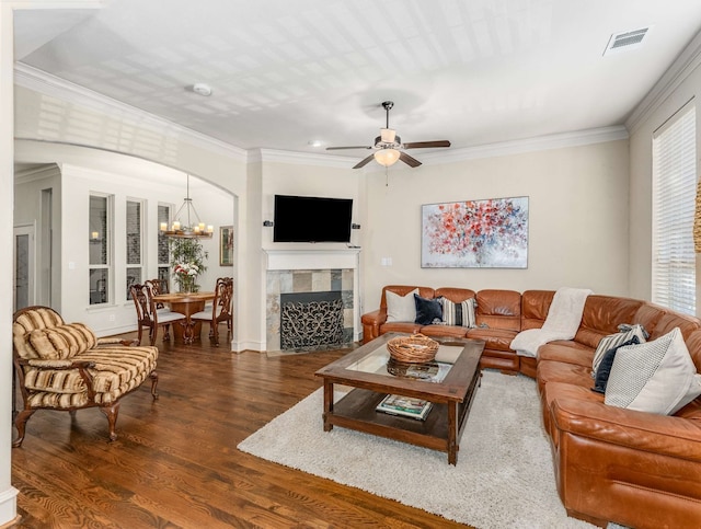 living room featuring a tile fireplace, ceiling fan with notable chandelier, crown molding, and dark wood-type flooring