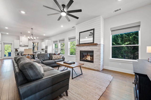 living room featuring ceiling fan with notable chandelier, wood-type flooring, and a fireplace