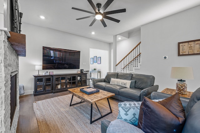 living room featuring hardwood / wood-style flooring, ceiling fan, and a stone fireplace