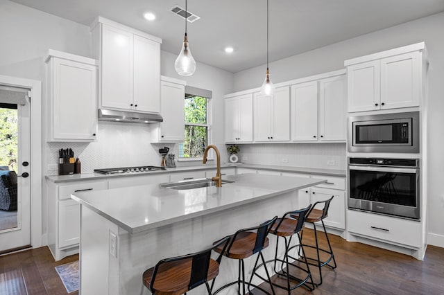 kitchen with sink, stainless steel appliances, an island with sink, pendant lighting, and white cabinets