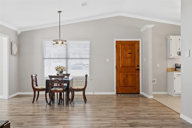 dining space with light hardwood / wood-style flooring, crown molding, and vaulted ceiling