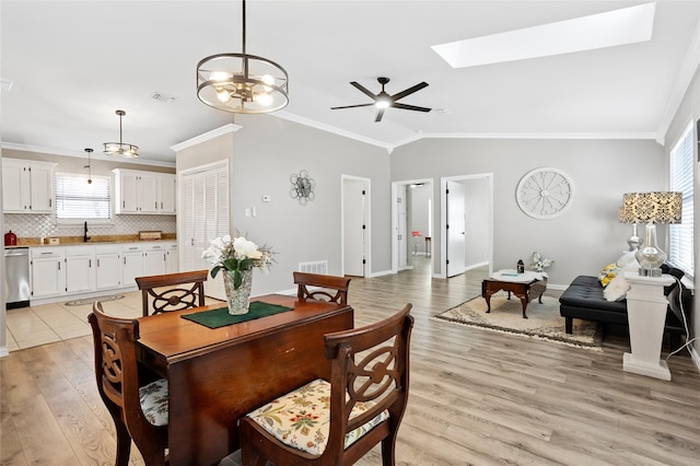 dining room featuring crown molding, vaulted ceiling with skylight, and light hardwood / wood-style flooring