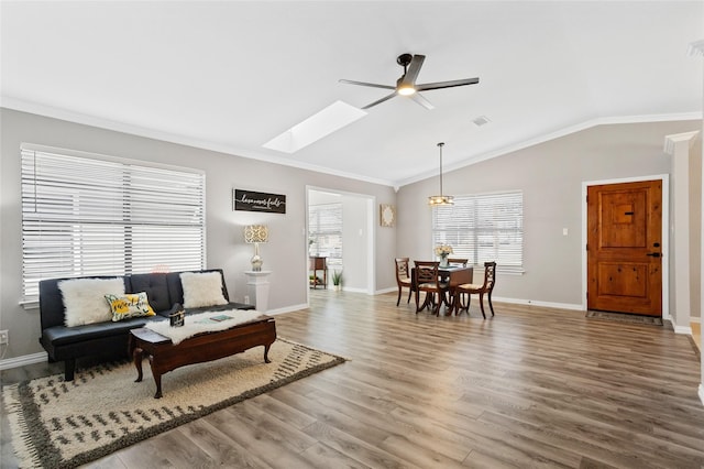 living room featuring hardwood / wood-style floors, ceiling fan, lofted ceiling with skylight, and crown molding