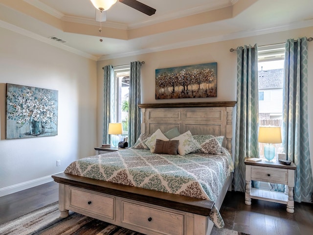 bedroom with dark hardwood / wood-style floors, a tray ceiling, and crown molding