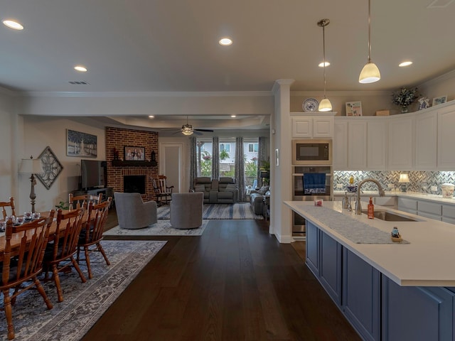 kitchen featuring sink, black microwave, pendant lighting, a fireplace, and white cabinets