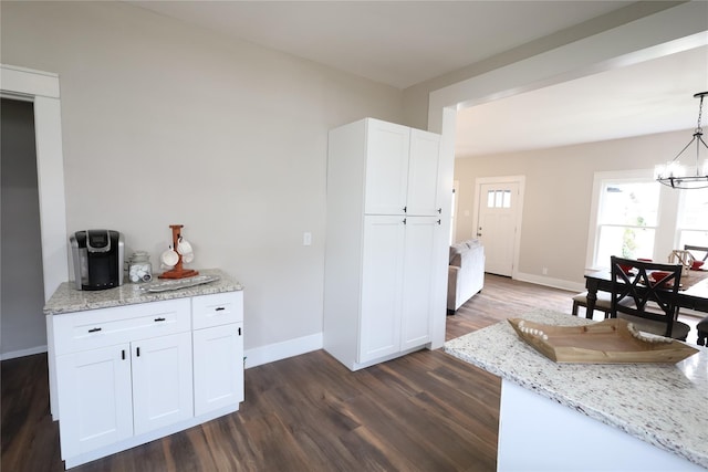 kitchen with dark wood-type flooring, hanging light fixtures, light stone counters, white cabinetry, and a chandelier