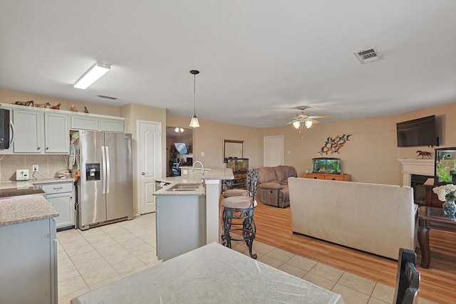 kitchen featuring stainless steel refrigerator with ice dispenser, a breakfast bar, ceiling fan, light tile patterned floors, and decorative light fixtures