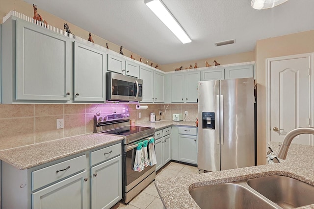 kitchen featuring gray cabinetry, sink, stainless steel appliances, decorative backsplash, and light tile patterned floors