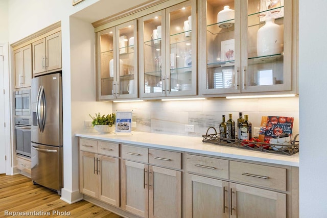 bar featuring decorative backsplash, appliances with stainless steel finishes, and light hardwood / wood-style flooring