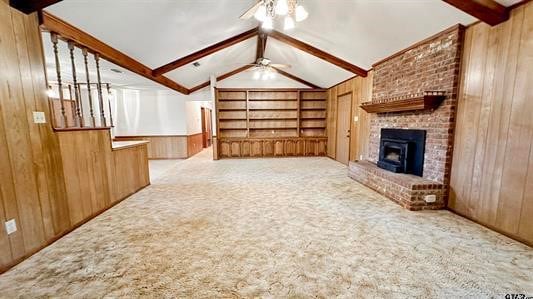 unfurnished living room featuring light carpet, vaulted ceiling with beams, ceiling fan, and wood walls