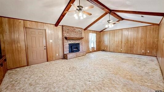 unfurnished living room with light carpet, ceiling fan, wooden walls, a fireplace, and vaulted ceiling with beams