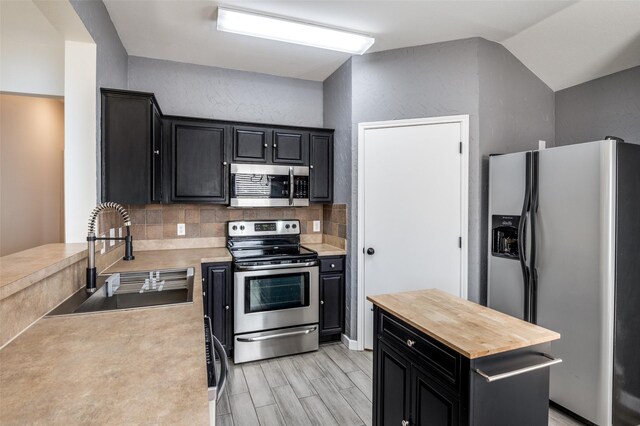 kitchen with sink, light hardwood / wood-style flooring, backsplash, vaulted ceiling, and appliances with stainless steel finishes